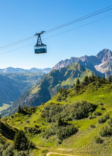 Bergbahn fährt über grüne Hänge und Berge im Kleinwalsertal, mit einem klaren blauen Himmel im Hintergrund. | © Oberstdorf · Kleinwalsertal Bergbahnen