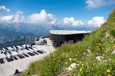 Bergbahnstation an der Nebelhorngipfelstation mit Aussicht auf die Berge, Sonnenterrasse mit Sonnenliegen und blühende Wiese im Vordergrund, Berglandschaft im Hintergrund. | © Oberstdorf · Kleinwalsertal Bergbahnen