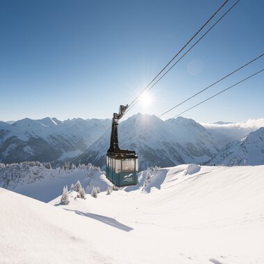Gondola lift in a winter landscape with snow-covered mountains and clear sunlit sky. | © Oberstdorf · Kleinwalsertal Bergbahnen