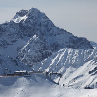 Schneebedeckte Berglandschaft mit einer Bergbahn im Vordergrund, umgeben von hohen, schneebedeckten Gipfeln. | © Oberstdorf · Kleinwalsertal Bergbahnen