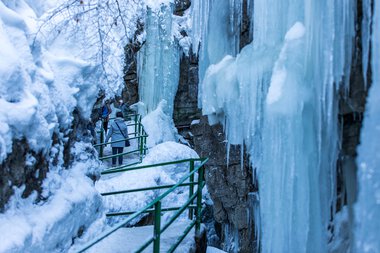 Winterliche Szene in der Breitachklamm mit gefrorenem Wasser und Menschen, die die Eiskulisse entlang eines abgestuften Weges erkunden. | © Kleinwalsertal Tourismus eGen • Breitachklamm • Fotograf: Frank Drechsel