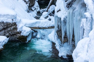 Bach in der Breitachklamm im Winter, umgeben von gefrorenem Wasser und Schnee, mit eisbedeckten Felsen und Eiszapfen. | © Kleinwalsertal Tourismus eGen • Breitachklamm • Fotograf: Frank Drechsel