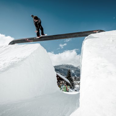 Skateboarder springt über eine Schneeschneise mit Schnee an den Seiten, bei klarer Himmel. Das Bild zeigt eine Winterszene auf einer Skipiste. | © Kleinwalsertal Tourismus eGen • Crystal Ground • Fotograf: Stefan Eigner
