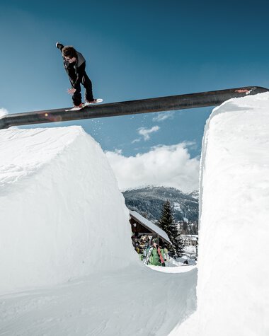 Skateboarder springt über eine Schneeschneise mit Schnee an den Seiten, bei klarer Himmel. Das Bild zeigt eine Winterszene auf einer Skipiste. | © Kleinwalsertal Tourismus eGen • Crystal Ground • Fotograf: Stefan Eigner