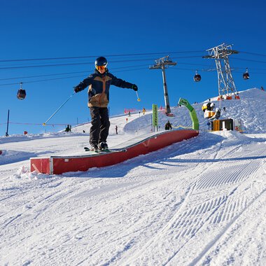Skifahrer beim Springen auf einem Schneekurven-Abschnitt in OBERSTDORF KLEINWALSERTAL, mit Skiliften und Pisten im Hintergrund. | © Kleinwalsertal Tourismus eGen • Oberstdorf Kleinwalsertal Bergbahnen