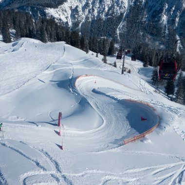 Schneebedektes Wintersportgebiet mit Kurven und Lawinenzaun, umgeben von Wald und Bergen. | © Kleinwalsertal Tourismus eGen • Oberstdorf Kleinwalsertal Bergbahnen