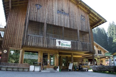 Holzverarbeiteter Hofladen mit Biohof-Beschilderung im Kleinwalsertal. Frontansicht mit Eingangsbereich, Velo und Sitzbänken. | © Kleinwalsertal Tourismus eGen • Biohof Feurerstein