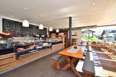 Innenansicht eines Hofladens mit Verkaufstheke, Tischen und Sitzgelegenheiten, viel Tageslicht, moderne Einrichtung. | © Kleinwalsertal Tourismus eGen • s´Hirscheck