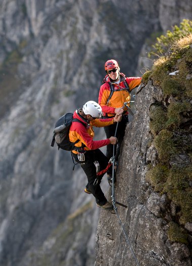 Zwei Kletterer beim Klettersteig in den Bergen, sichern sich an einer schmalen Felskante fest. | © Kleinwalsertal Tourismus eGen • Bergschule