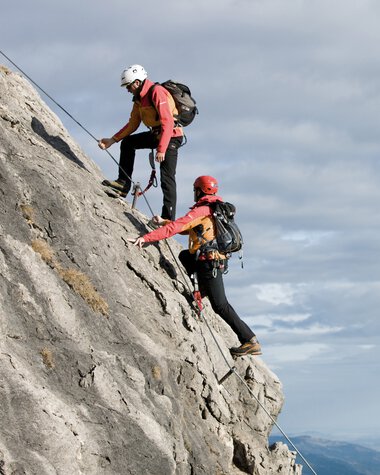 Zwei Kletterer steigen an einer steilen Felswand mit Kletterausrüstung und Helmen auf. Das Bild zeigt eine Klettertour im Kleinwalsertal. | © Kleinwalsertal Tourismus eGen • Bergschule
