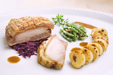Krustenbraten mit Blaukraut, Erdapfel-Roulade und grünen Bohnen auf einem weißen Teller. | ©  Kleinwalsertal Tourismus eGen • Fotograf: Werner Krug