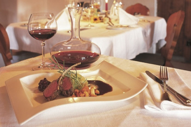 Kotelett von der Gams, serviert mit Rotwein, auf einem eleganten Esstisch im Alpenhof Jäger | © Kleinwalsertal Tourismus eGen • Alpenhof Jäger