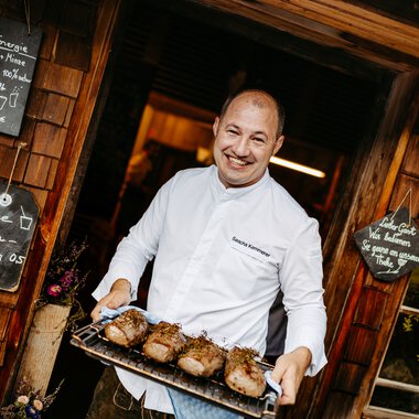 Mann in Gastronomie-Uniform trägt ein Tablett mit frisch gegrilltem Fleisch bei einem kulinarischen Festival im Kleinwalsertal. | © Kleinwalsertal Tourismus eGen • Photographer: Sascha Gast