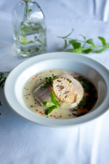 Ein elegantes Gericht mit einer kühlen Suppe, Garnelen und einer knusprigen Scheibe Brot, garniert mit frischen Minzblättern. | © Kleinwalsertal Tourismus eGen • Fotograf: Isenhoff