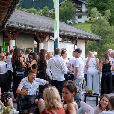 Menschen genießen ein kulinarisches Festival im Freien vor einem Gebäude mit traditioneller Holzarchitektur, im Grünen mit Hügeln und Häusern im Hintergrund. | © Kleinwalsertal Tourismus eGen • Fotograf: Isenhoff