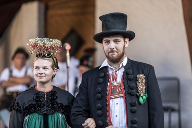 Ein Mann und eine Frau in traditionellen Trachten bei einem Alphornfestival, die Frau trägt einen Blumenkranz auf dem Kopf. | © Kleinwalsertal Tourismus eGen • Fotograf: Frank Drechsel