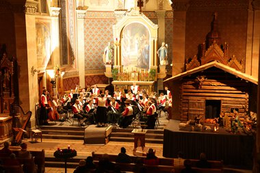 Musikkapelle bei einem Adventskonzert in einer Kirche, mit Orchester auf der Bühne und festlicher Dekoration im Hintergrund. | © Kleinwalsertal Tourismus eGen • Fotograf: Frank Drechsel