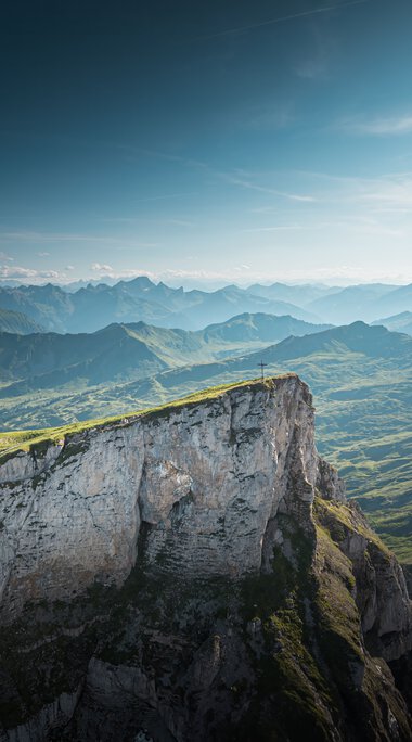 Berglandschaft mit grünen Hügeln und steilen Klippen unter einem blauen Himmel, aufgenommen vom Ifen.