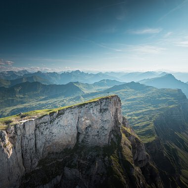 Berglandschaft mit grünen Hügeln und steilen Klippen unter einem blauen Himmel, aufgenommen vom Ifen. | © Kleinwalsertal Tourismus eGen • Fotograf: Robert Niederwolfsgruber