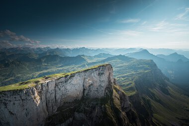 Berglandschaft mit grünen Hügeln und steilen Klippen unter einem blauen Himmel, aufgenommen vom Ifen.