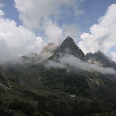 Berglandschaft mit schroffen Gipfeln, teilweise von Wolken bedeckt, in den Bergen. Eine beeindruckende Naturaufnahme.