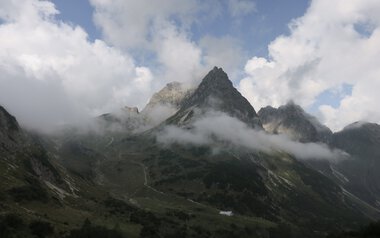Mountain landscape with rugged peaks partly covered by clouds, showcasing stunning natural scenery. | © Kleinwalsertal Tourismus eGen • Photographer: Antje Pabst