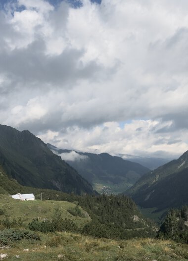 Berglandschaft mit Tal, bewölktem Himmel und grünen Hügeln in den Bergen.