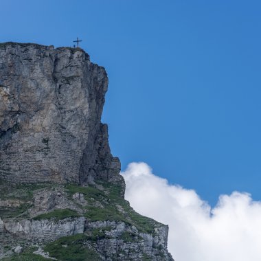Felsen am Gipfel des Ifen mit Gipfelkreuz vor blauem Himmel und Wolken im Sommer.