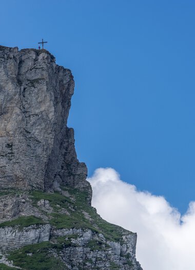 Felsen am Gipfel des Ifen mit Gipfelkreuz vor blauem Himmel und Wolken im Sommer.