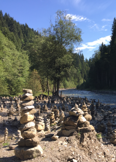 Wanderweg entlang eines Flusses in den österreichischen Alpen, umgeben von grünen Bäumen und Berglandschaft.