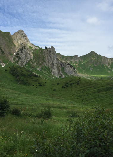 Grüne Wiesen im Bärguntal mit Bergen im Hintergrund, wolkiger Himmel, Sommer im Kleinwalsertal.