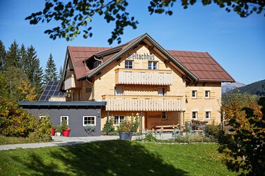 Das Bio-Hotel Breitachhus, ein charakteristisches Haus mit Holzverkleidung und Solaranlage, steht in einer grünen, bergigen Umgebung.