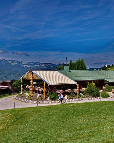 Bergstüble im Kleinwalsertal mit grüner Wiese, blauer Himmel und umliegende Berge, im Sommer bei gutem Wetter.