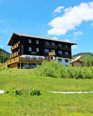 Modernes Gebäude in ländlicher Umgebung im Kleinwalsertal, umgeben von grünen Wiesen und Bergen, bei sonnigem Himmel.