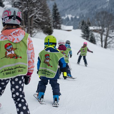 Kinder im Skikurs lernen das Skifahren auf einer verschneiten Piste mit Skilehrern und Eltern in Mittberg.