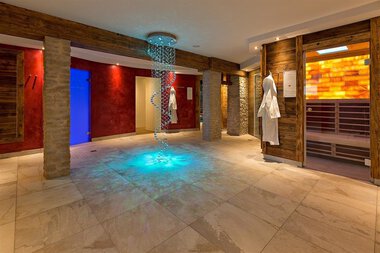 Innenraum eines Spa- oder Wellnessbereichs mit Wasserfall, ansprechender Beleuchtung und Saunapositionen.