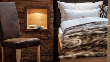 © Pro Vision Media Innenansicht eines gemütlichen Zimmers mit einem Bett, Kopfteil in Schwarz, und einer Holzbox an der Wand, die ein Buch enthält.