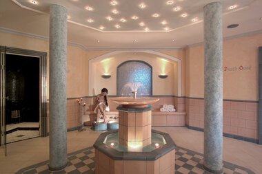 Innenraum eines Wellnesshotels mit einer Wasserfontäne in der Mitte, Wasserbecken und ruhiger Atmosphäre.