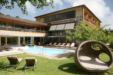 Das Naturhotel Chesa Valisa mit Außenpool, Liegestühlen und Garten im Sonnenlicht, umgeben von Bäumen.