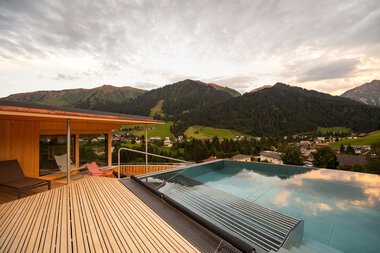Panoramaaufnahme eines Hotel-Pools auf einer Deckterrasse mit Blick auf Berge und grüne Landschaft bei Sonnenuntergang.