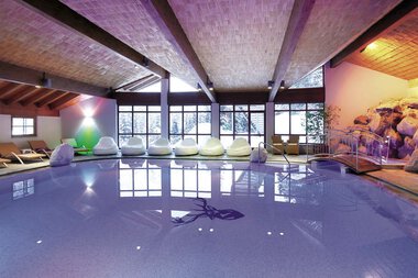 Innenaufnahme eines Wellnessbereichs mit einem Pool, Liegen und Fenster, die viel Tageslicht hineinlassen.