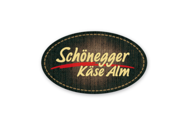 Das Logo von Schönegger Käse Alm, oval mit dunklem Hintergrund und gelber, roter und weißer Schrift.