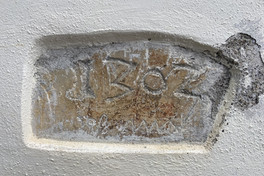 Alter Stein mit eingeschnittenem Text 'IZBOZ' und unleserlichen Zeichen, in eine Wand eingelassen.