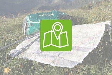 Eine Wanderkarte liegt auf grünem Gras, neben einer grünen Tasche, mit einer Markierung, die den Orientierungspunkt zeigt.