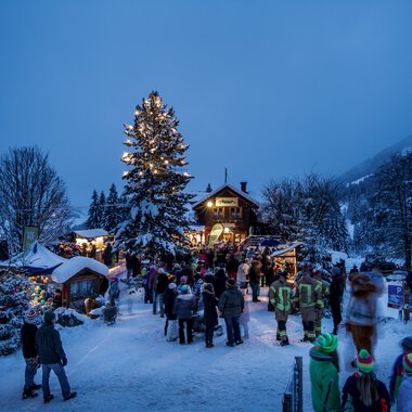 Festliche Winterveranstaltung am Adventszauber mit Besuchern, Weihnachtsbäumen und festlichem Lichterglanz in einer verschneiten Landschaft.