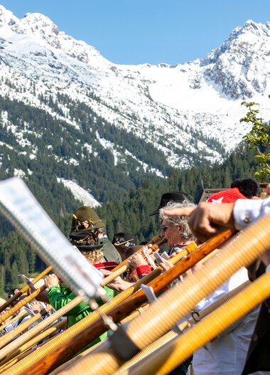 Musiker beim Alphornfestival in den Bergen mit Schneegipfeln im Hintergrund. | © Kleinwalsertal Tourismus eGen • Fotograf: Frank Drechsel