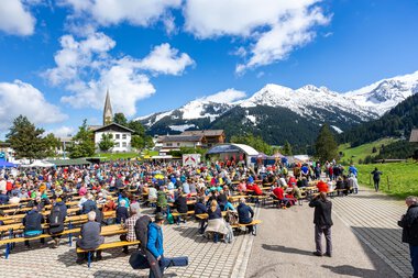 Großes Alphornfestival im malerischen Bergdorf mit vielen Besuchern, Bergen und blauer Himmel im Hintergrund.