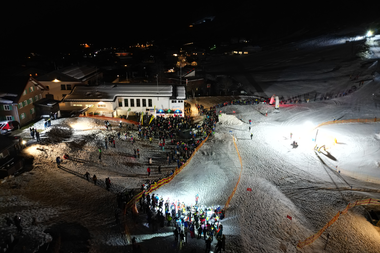 Abendliche Skispaß-Szene mit vielen Menschen auf den Pisten des Kleinwalsertals, beleuchtet bei Nacht.