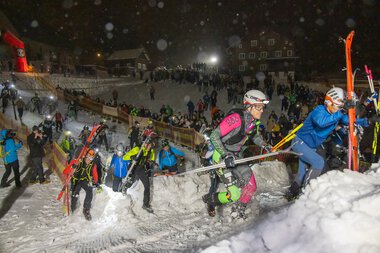 Menschen beim Schneeschuhtrekking bei der Veranstaltung 'Bock uf Steil' im Winter 2025, in einer verschneiten Bergregion, umgeben von Häusern und einer Menschenmenge.