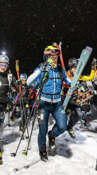 Group of skiers at night in the snow, equipped with skis and ski boots, participating in an event.